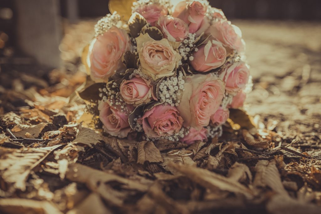 Brautstrauß liegt auf herbstlichen Blättern hinter Hochzeitsringen