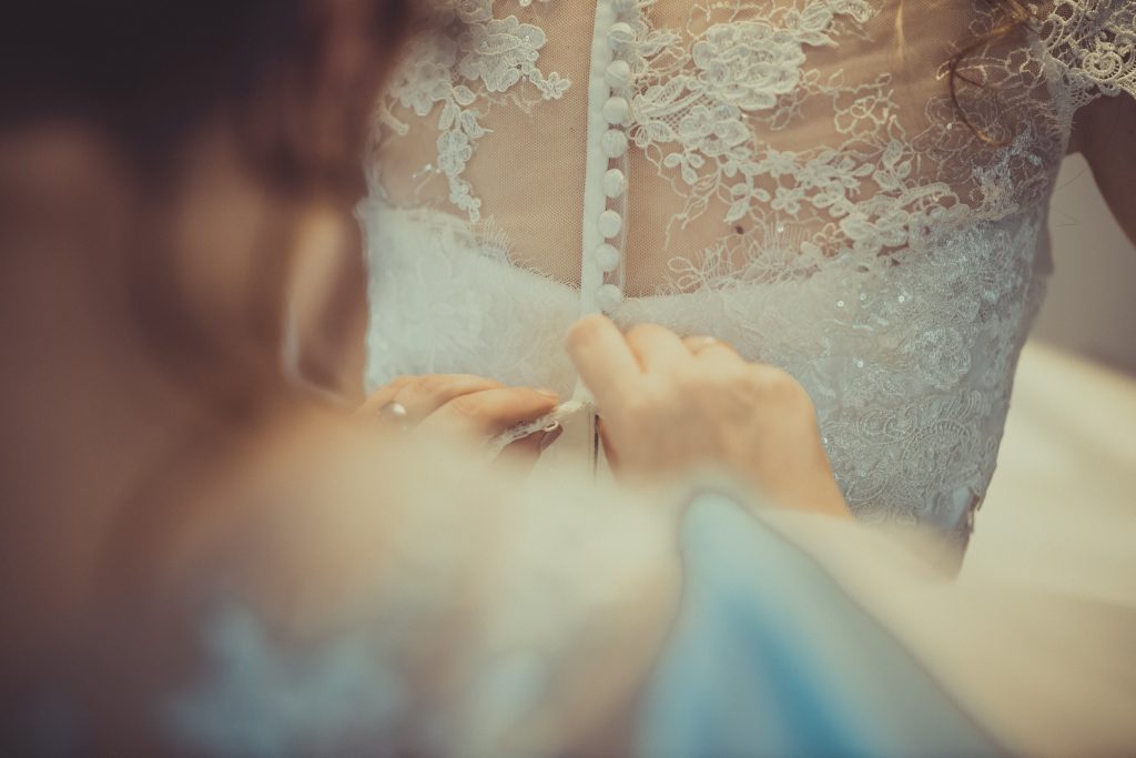 Trauzeuge knöpft der Braut das Hochzeitskleid zu