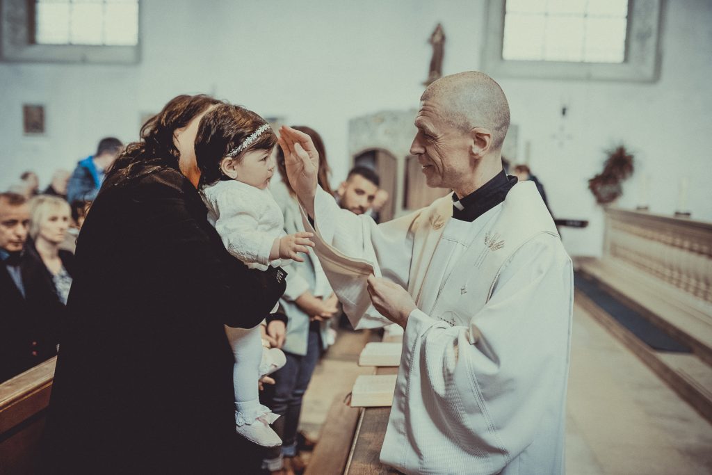 Priester oder Pfarrer gratuliert den Taufeltern zur Taufe und tauft das Kind