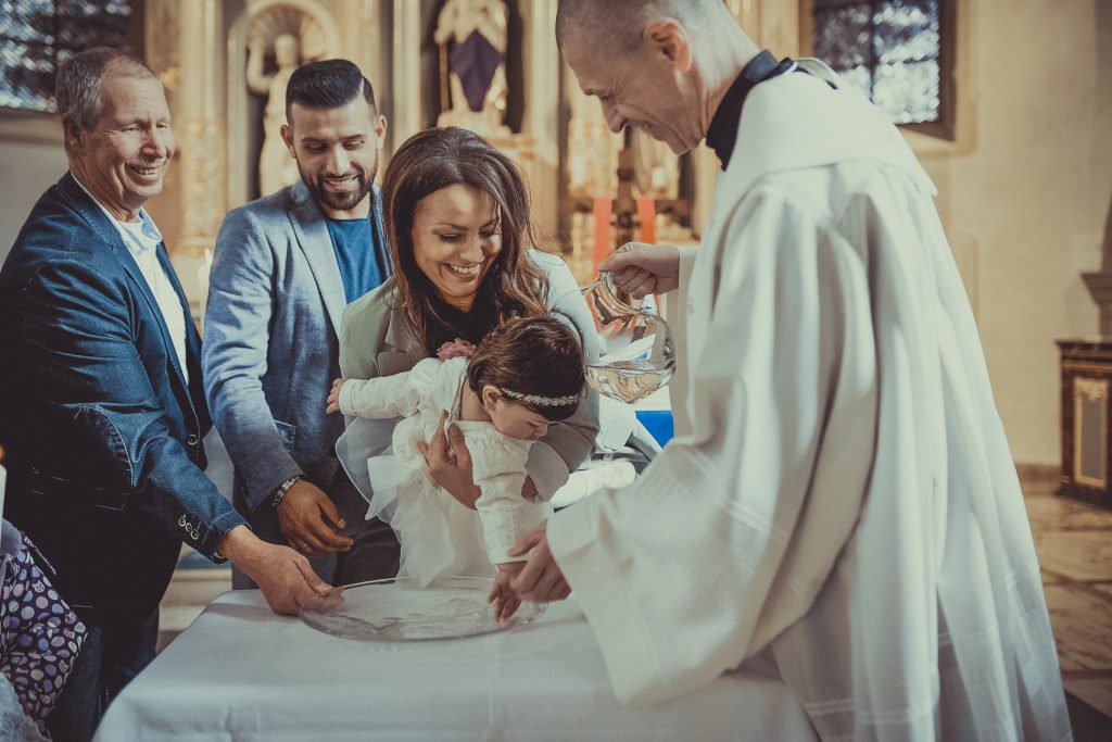 Priester oder Pfarrer gratuliert den Taufeltern zur Taufe und tauft das Kind