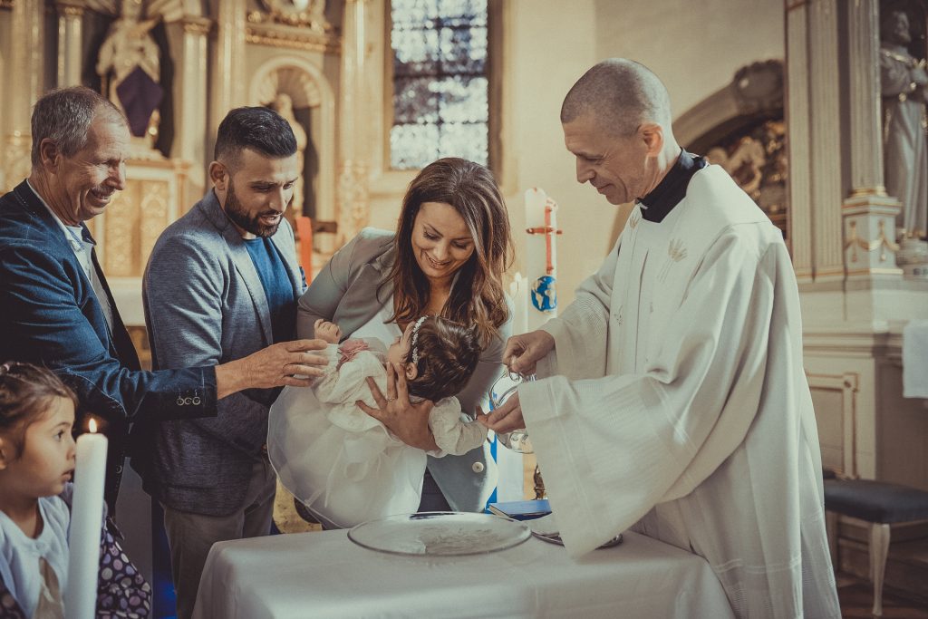 Priester oder Pfarrer gratuliert den Taufeltern zur Taufe und tauft das Kind