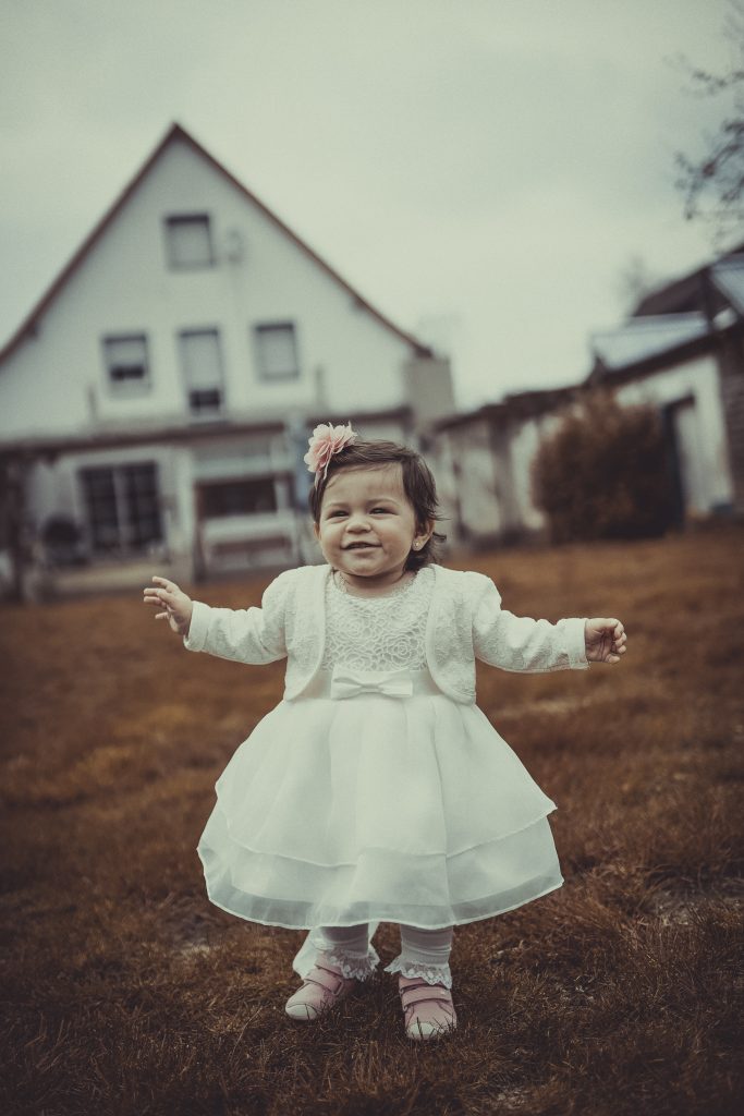 Taufkind läuft mit Taufkleid und Taufschleife
